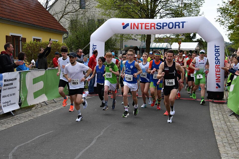 Eine Gruppe von Läufern startet einen Wettlauf unter einem großen Zelt mit dem Logo von Intersport. Im Hintergrund stehen Zuschauer und feiern die Teilnehmer. | © MSC Bad Blumau Lauffestival