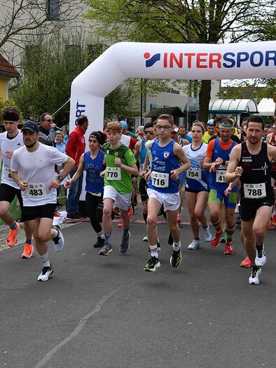 A group of runners is starting a race under a large tent with the Intersport logo. In the background, spectators are standing and celebrating the participants. | © MSC Bad Blumau Lauffestival