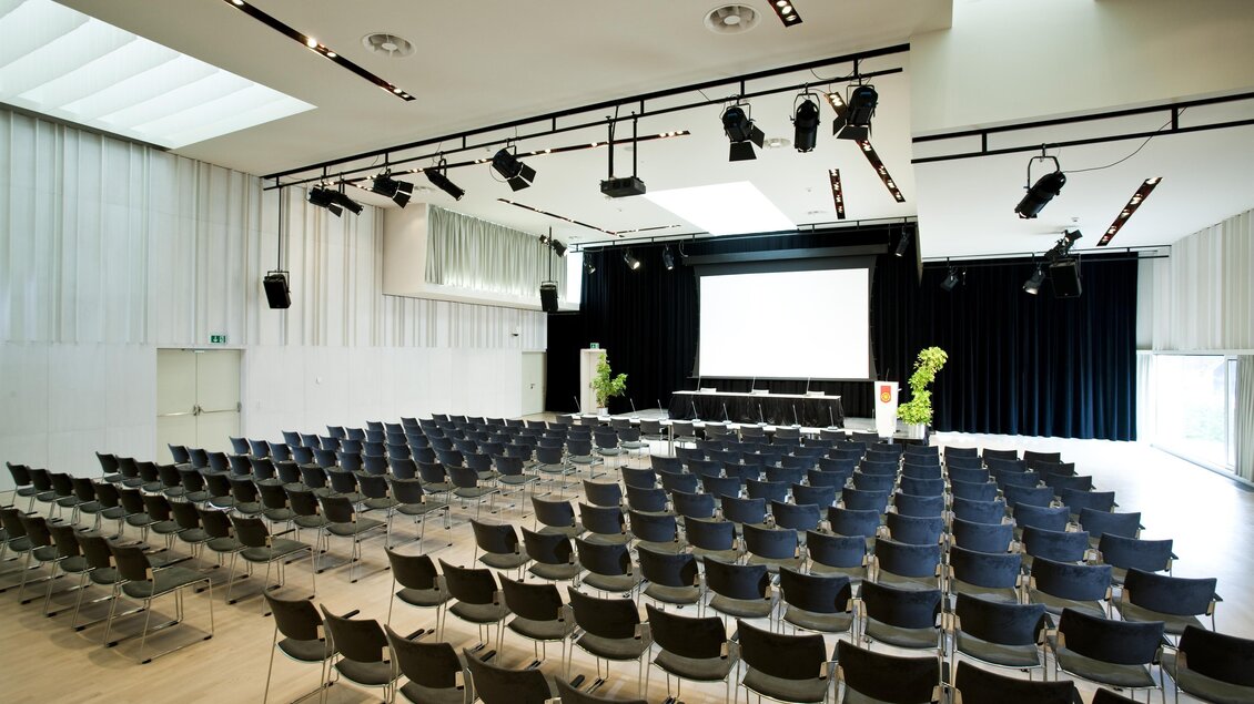Ein moderner Veranstaltungsraum mit vielen Stühlen in Reihen. Eine große Leinwand und einige Pflanzen sind sichtbar. | © Zehnerhaus Bad Radkersburg
