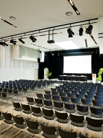 Ein moderner Veranstaltungsraum mit vielen Stühlen in Reihen. Eine große Leinwand und einige Pflanzen sind sichtbar. | © Zehnerhaus Bad Radkersburg