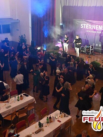 A festive event with dancing guests in formal attire. In the background, a band plays on a stage with colorful lights. | ©  FF Leoben-Stadt