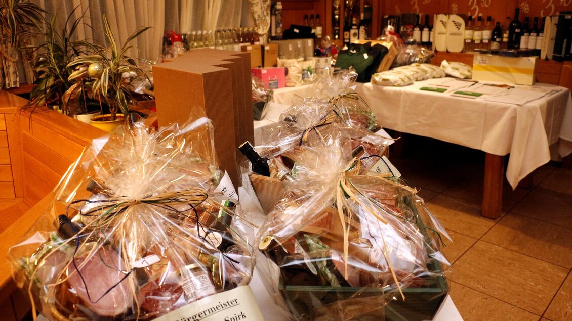 Zwei Geschenkkörbe mit dekorativem Cellophan auf einem Tisch. Im Hintergrund sind weitere Produkte und Weinflaschen sichtbar. | © FF Bad Loipersdorf
