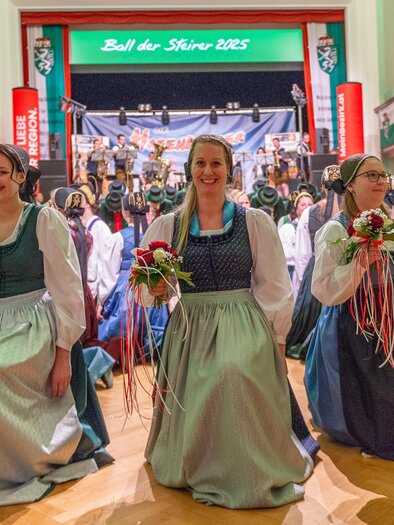 A festive event with several women wearing traditional costumes. In the background, there is a stage with a band and many spectators. | © Picwish, Robert Tüchi