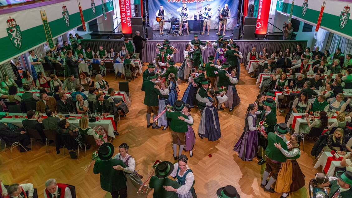 Eine traditionelle Tanzveranstaltung mit vielen Menschen in bunten Trachten. Im Hintergrund spielt eine Band und die Atmosphäre ist festlich und lebhaft. | © Picwish, Robert Tüchi