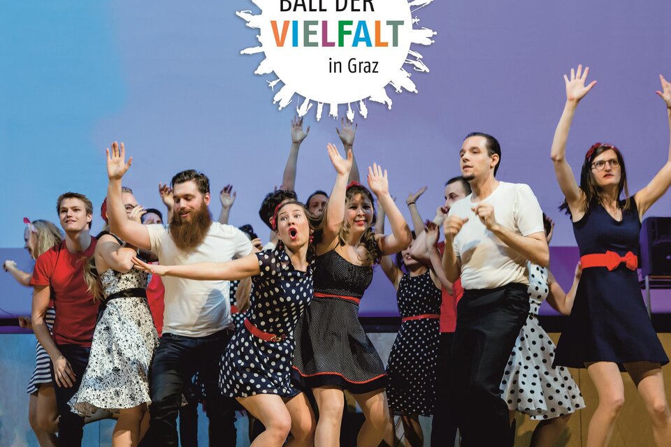 Eine Gruppe von Menschen tanzt und singt auf einer Bühne. Sie tragen festliche Kleidung und die Stimmung ist fröhlich. | © Ball der Vielfalt