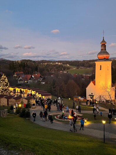 People visit the Bartholomew Advent Market with church and lights at dusk. | © Josef Birnstingl