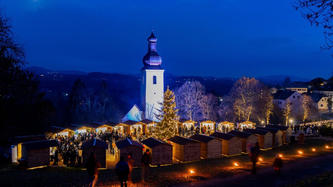 Adventmarkt in St. Bartholomä mit beleuchteten Hütten und Kirche bei Dunkelheit. | © Harry Schiffer