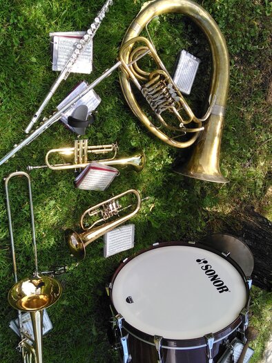 A collection of musical instruments lies on green grass. Visible are a tuba, trumpets, a trombone, a flute, and a drum. | © Marlene Zandl