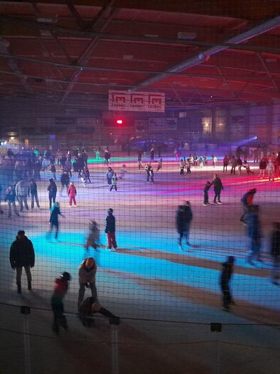 A busy ice rink with many people skating on the ice. Colorful lights create a festive atmosphere. | © Ralf Moder/ Facebook