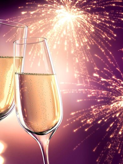 Zwei Sektgläser stoßen auf einen festlichen Anlass an, umgeben von bunten Feuerwerken. Der Hintergrund ist mit weichen Lichtern geschmückt und strahlt Freude aus. | © Fotalia