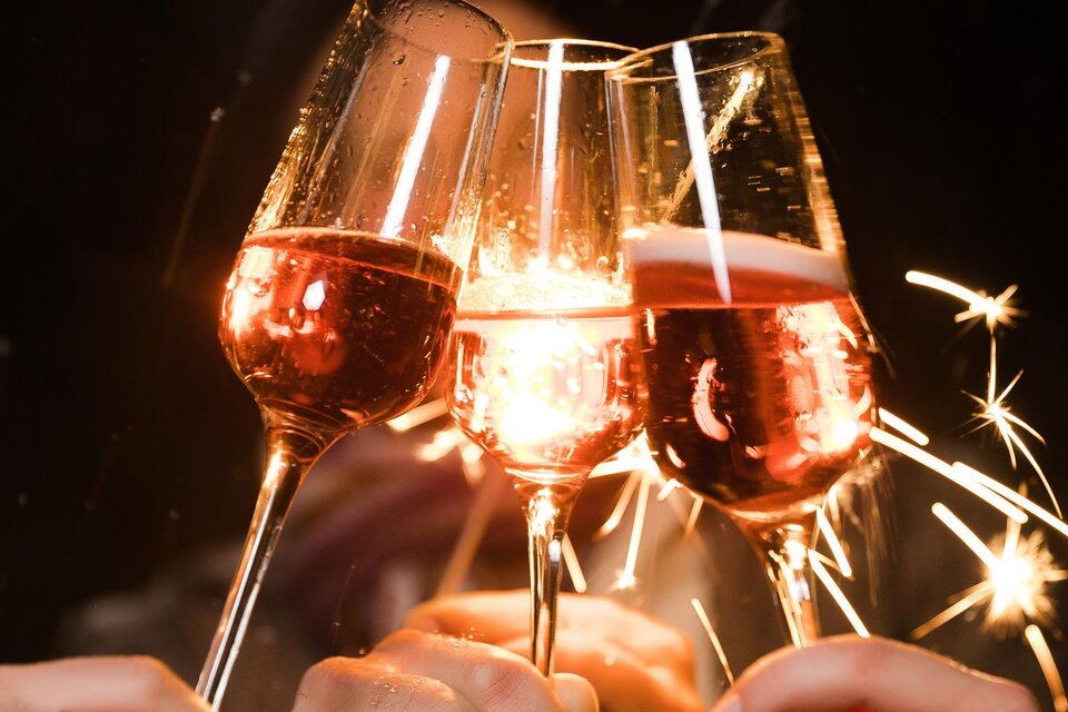 Drei Gläser mit roséfarbigem Getränk stoßen an, umgeben von funkelnden Wunderkerzen. Die Atmosphäre ist festlich und feierlich. | © Lupi Spuma