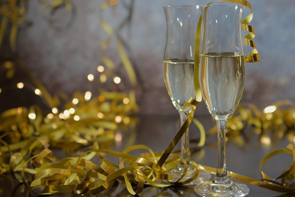 Zwei Sektgläser mit sprudelndem Getränk stehen auf einem Tisch. Um die Gläser liegen goldene Dekoration und Reste von Feierlichkeiten. | © Pixabay