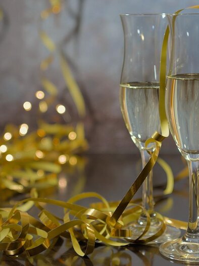 Zwei Sektgläser mit sprudelndem Getränk stehen auf einem Tisch. Um die Gläser liegen goldene Dekoration und Reste von Feierlichkeiten. | © Pixabay