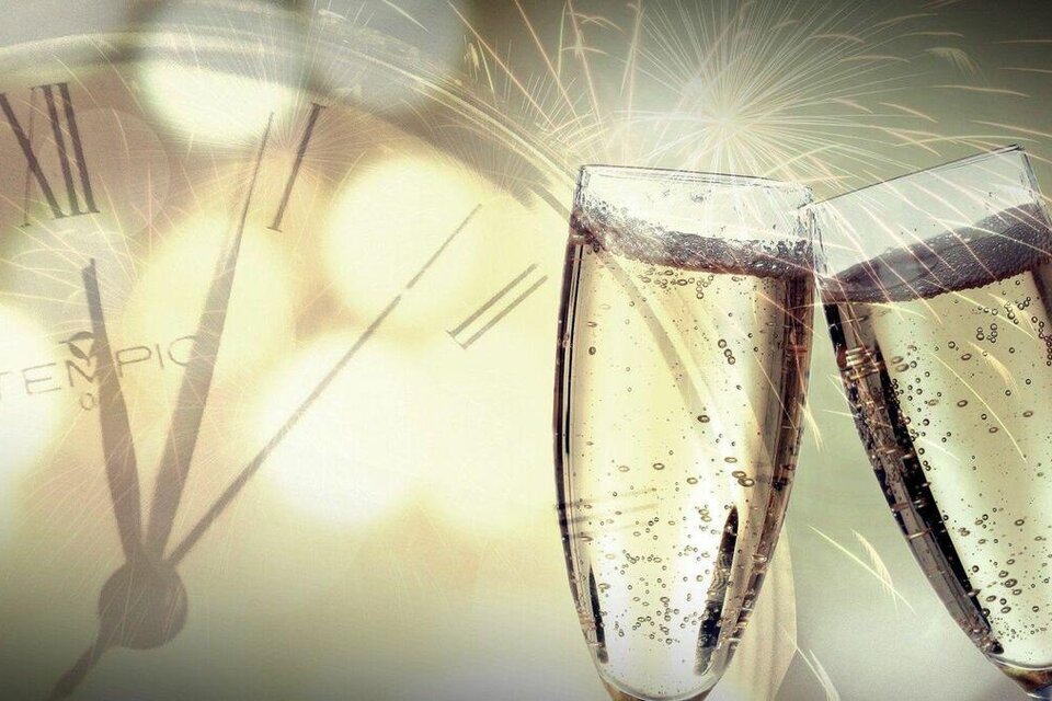 Zwei Gläser Sekt stoßen an, während im Hintergrund eine Uhr und Feuerwerk zu sehen sind. Die Atmosphäre ist festlich und feierlich. | © Pixabay