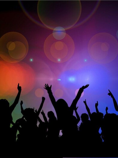 A group of people is dancing and celebrating in front of colorful lights. The silhouettes convey joy and movement in a festive atmosphere.