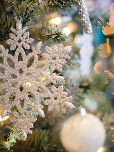 Ein glitzernder Schneeflockenanhänger hängt an einem Weihnachtsbaum. Im Hintergrund leuchten bunte Lichter. | © pixabay.com