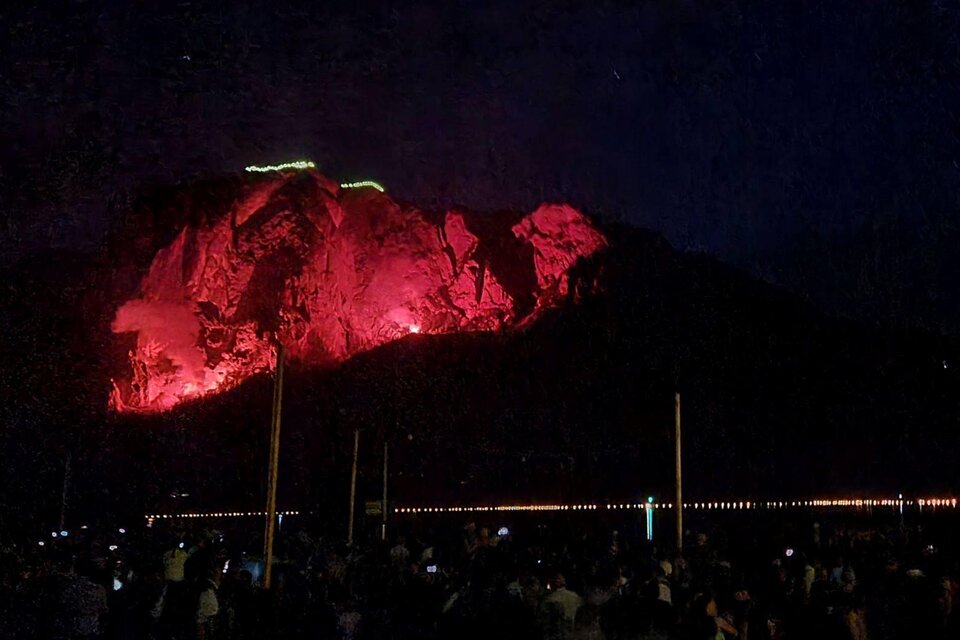 Ein großer Berg wird nachts von rotem Licht beleuchtet. Darunter versammeln sich viele Menschen, die das Spektakel beobachten. | ©  Stephanie Bor