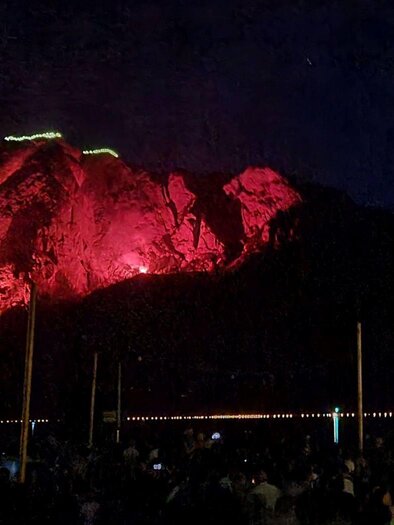 A large mountain is illuminated by red light at night. Below, many people gather to watch the spectacle. | ©  Stephanie Bor
