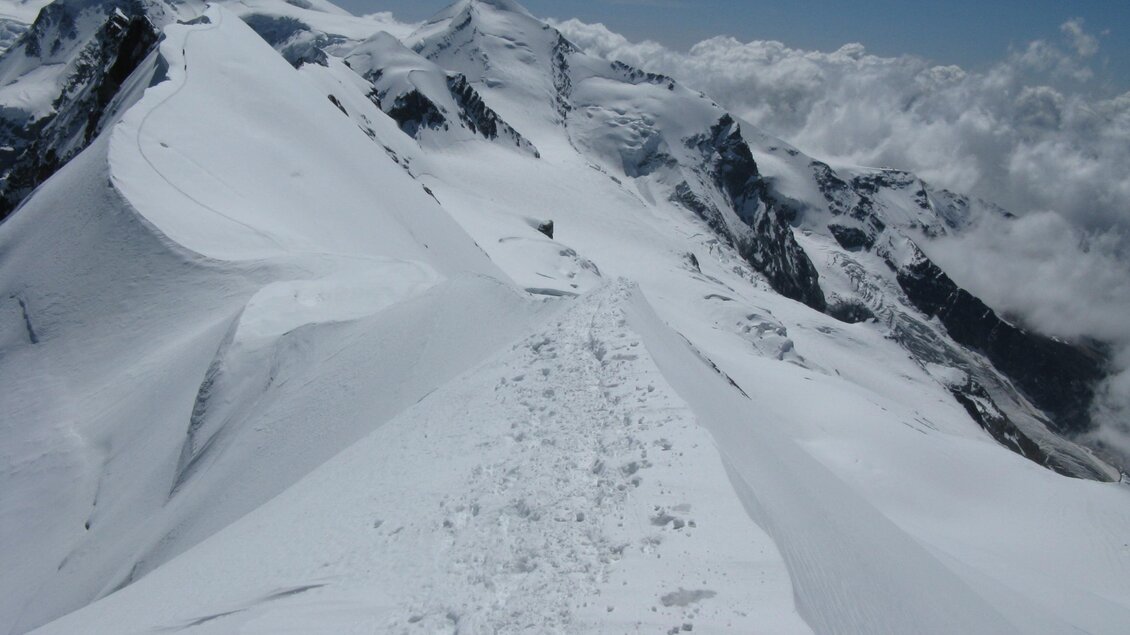 Eine schneebedeckte Berglandschaft mit klaren, blauen Himmel. Der schmale Pfad führt über die Gipfel, umgeben von beeindruckenden Wolken. | © Kager Eduard