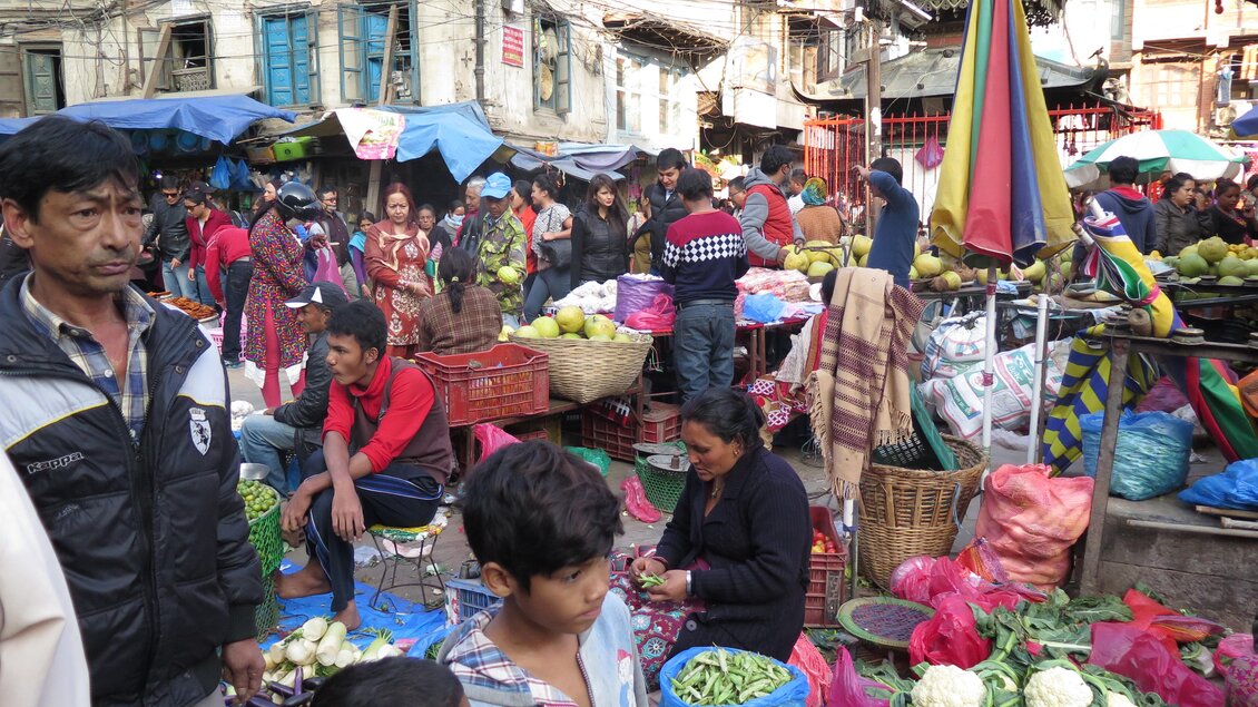 Ein lebhafter Markt mit vielen Menschen, die frisches Obst und Gemüse verkaufen. Bunte Stände und Einkaufskörbe prägen die Szene. | © Kager Eduard