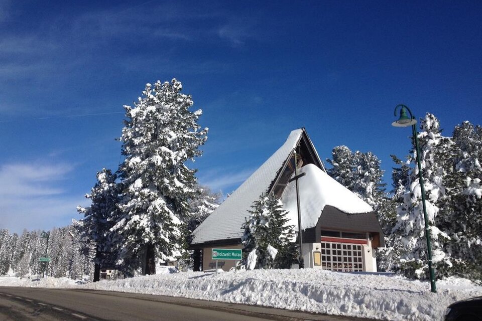Eine verschneite Landschaft mit einem markanten Gebäude und hohen, schneebedeckten Bäumen. Der Himmel ist klar und blau. | © TV Turracher Höhe 