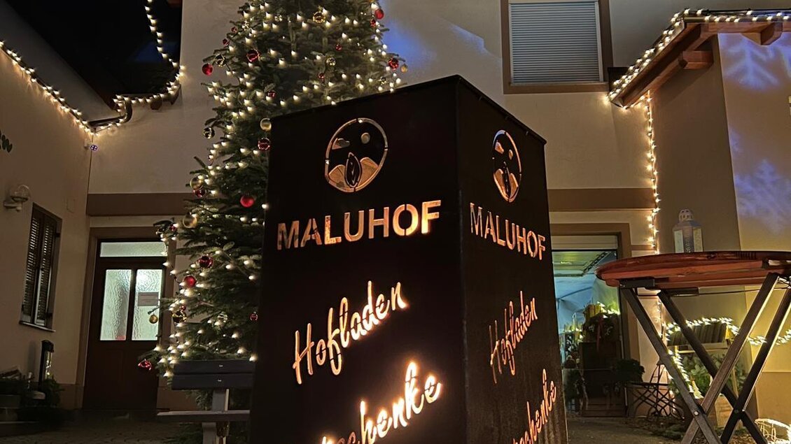 Ein festlich dekorierter Innenhof mit einem Weihnachtsbaum und Lichtern. Im Vordergrund steht ein beleuchteter stummer Diener mit dem Schriftzug "MaluHof". | © MALU