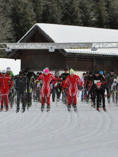 A group of skiers starts a race on a snow slope. In the background, trees and a building can be seen. | © Georg Petritsch
