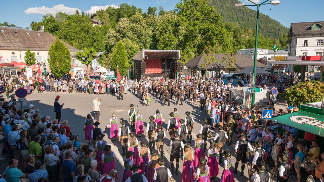 Eine lebendige Veranstaltung mit vielen Menschen, die sich um eine Bühne versammeln. Hinter der Menge sind grüne Berge zu sehen, die die Szenerie umrahmen. | © Narzissenfestverein