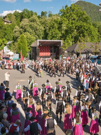 A lively event with many people gathering around a stage. In the background, green mountains can be seen, framing the scene. | © Narzissenfestverein