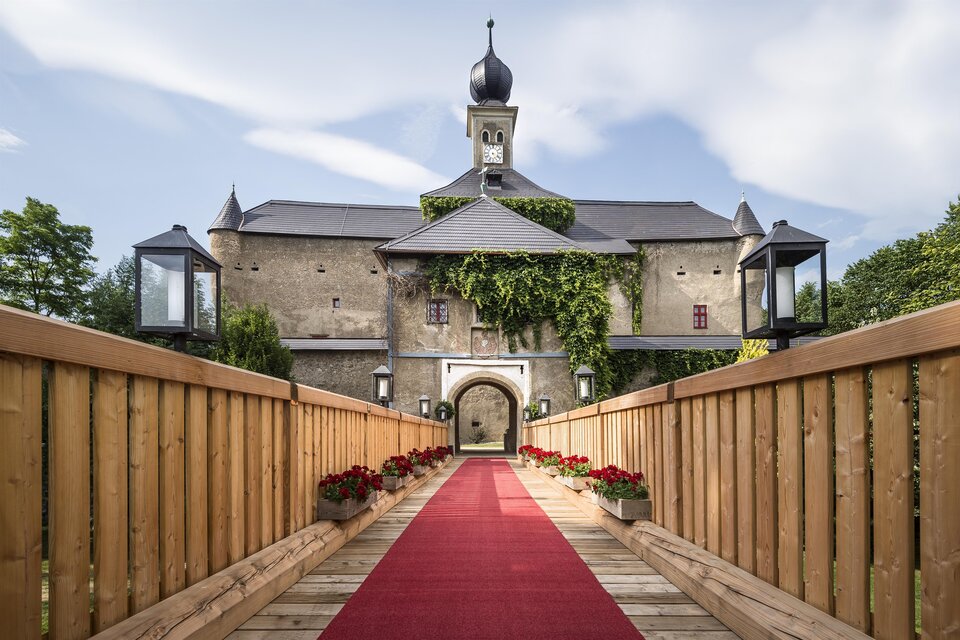Ein beeindruckendes Schloss mit einer roten Teppichzufahrt. Die Fassade ist mit Pflanzen bedeckt und von Laternen gesäumt. | © Tauroa GmbH