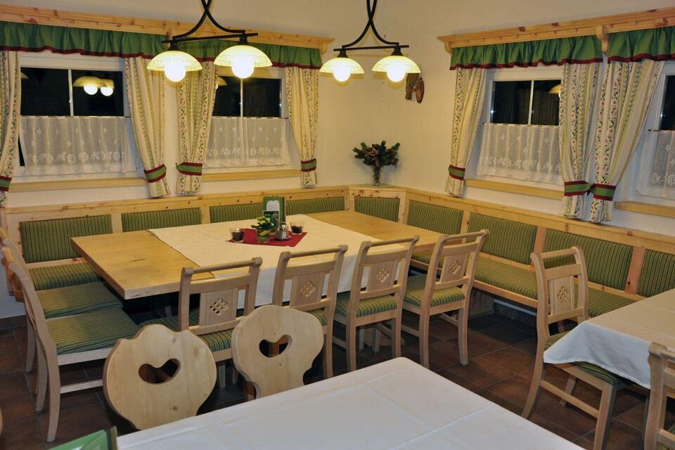 Ein gemütlicher Essbereich mit einem großen Tisch und Bänken. Die Wände sind mit Vorhängen und dekorativen Elementen in traditionellem Stil gestaltet. | © Poppnangerl