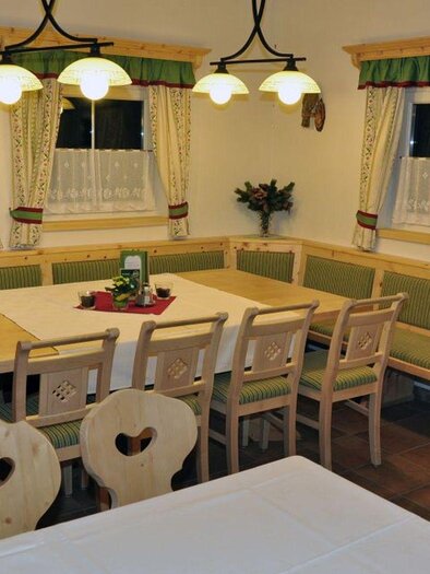 Ein gemütlicher Essbereich mit einem großen Tisch und Bänken. Die Wände sind mit Vorhängen und dekorativen Elementen in traditionellem Stil gestaltet. | © Poppnangerl