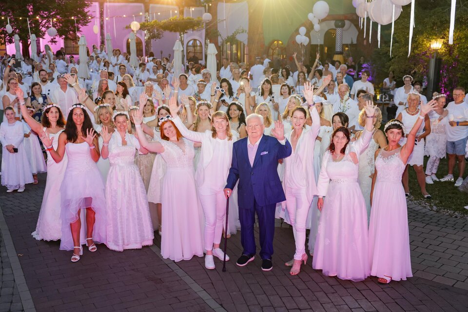 Eine große Gruppe von Menschen in weißen Kleidern feiert zusammen. Sie stehen in einem festlichen Ambiente und scheinen Freude zu haben. | © Sarah Raiser