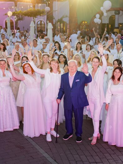 A large group of people in white dresses is celebrating together. They stand in a festive atmosphere and seem to be having joy. | © Sarah Raiser