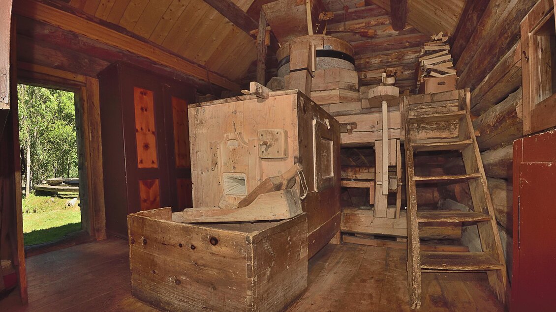 Ein rustikales Holzinterieur mit einer alten Maschinenanordnung. Im Hintergrund sind Holzstapel und eine Treppe zu sehen. | © Naturpark Sölktäler