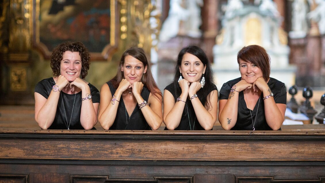 Vier Frauen lächeln und posieren freundlich an einem Tisch. Der Hintergrund zeigt eine beeindruckende Innenarchitektur. | © Die Zwitschertanten