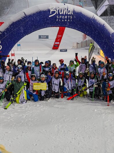 A group of skiers celebrates at a competition in the snow. They are standing under a large blue-and-white gate and have a map in the center. | © Steirischer Skiverband