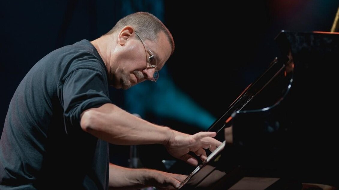 Ein Pianist spielt konzentriert am Klavier. Im Hintergrund sind verschwommene Lichter zu sehen. | © Tom Hejan