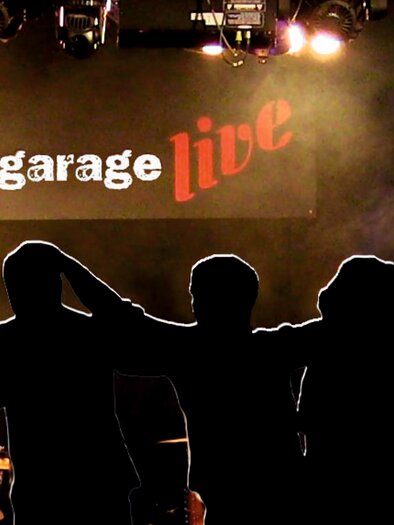 Silhouetten von fünf Personen stehen vor einer Bühne. Im Hintergrund ist ein beleuchtetes Banner mit der Aufschrift "bluegarage live" zu sehen.