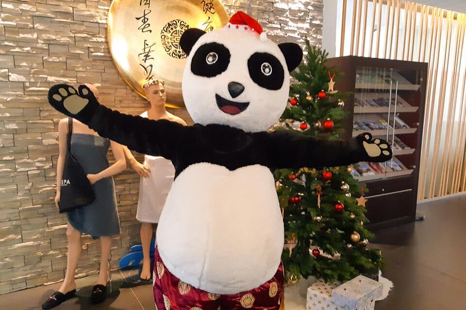 Ein Panda-Kostüm steht fröhlich vor einem Weihnachtsbaum und lächelt. Im Hintergrund sind Schaufensterpuppen zu sehen. | © Asia Hotel & Spa Leoben
