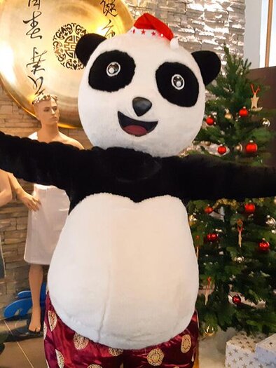 A panda costume stands cheerfully in front of a Christmas tree and smiles. In the background, mannequins can be seen. | © Asia Hotel & Spa Leoben