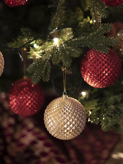 A festively decorated Christmas tree with colorful ornaments in red and gold. Softly glowing lights can be seen in the background. | © Pixabay.com