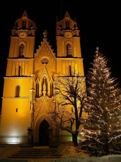 Eine beeindruckende Kirche mit zwei Türmen leuchtet in der Nacht. Neben der Kirche steht ein festlich geschmückter Weihnachtsbaum.