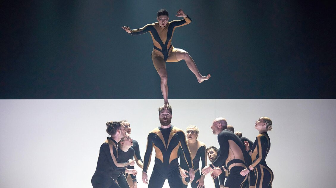 Neun Artisten und Artistinnen stehen konzentriert beisammen, einer macht einen Handstand am Kopf eines Kollegen im Cirque Noël in Graz.  | © Andy Phillipson