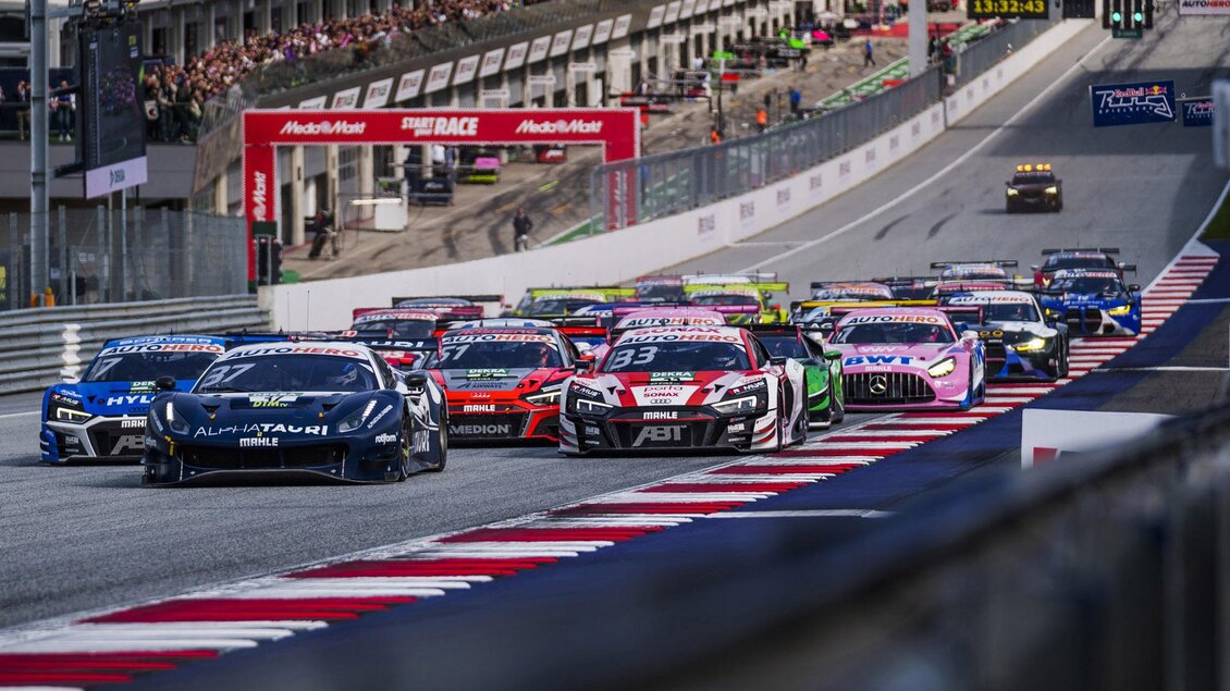 Ein spannendes Autorennen auf einer Rennstrecke mit mehreren Autos, die nebeneinander fahren. Im Hintergrund sind Zuschauer und Boxen zu sehen. | © Philip Platzer Red Bull Ring