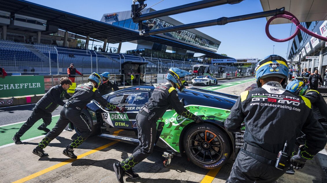 Ein Formel-1-Rennwagen wird in die Box geschoben, während ein Team von Mechanikern bei der Arbeit ist. Die Szene zeigt intensiven Rennsport mit klarer blauer Himmel und einer modernen Rennstrecke im Hintergrund. | © Red Bull Ring