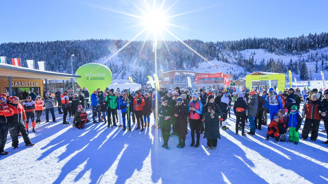 Eine große Gruppe von Menschen versammelt sich im Schnee unter klarem blauen Himmel. Die Sonne scheint hell und wirft lange Schatten auf den Boden. | © Michael Simonlehner