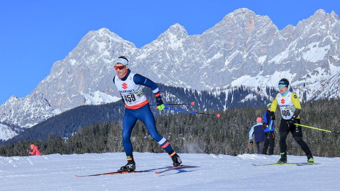 Zwei Langläufer trainieren auf einer verschneiten Piste in montanem Gebiet. Im Hintergrund sind hohe Berge und ein klarer blauer Himmel zu sehen. | © Michael Simonlehner