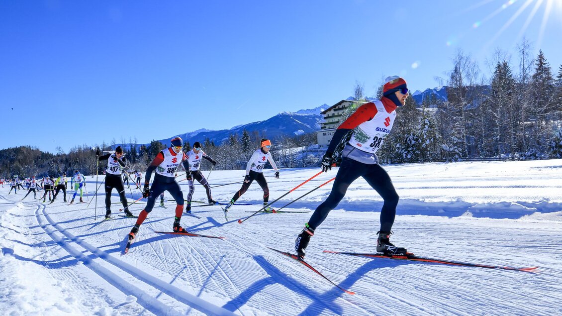 Eine Gruppe von Langläufern bewegt sich auf einer schneebedeckten Strecke. Im Hintergrund sind Berge und ein klarer blauer Himmel zu sehen. | © Michael Simonlehner