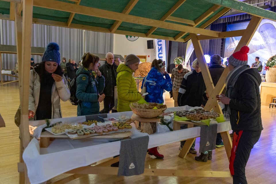 Ein festlicher Stand mit verschiedenen Snacks und Leckereien. Menschen stehen zusammen und genießen die Atmosphäre. | © Michael Simonlehner